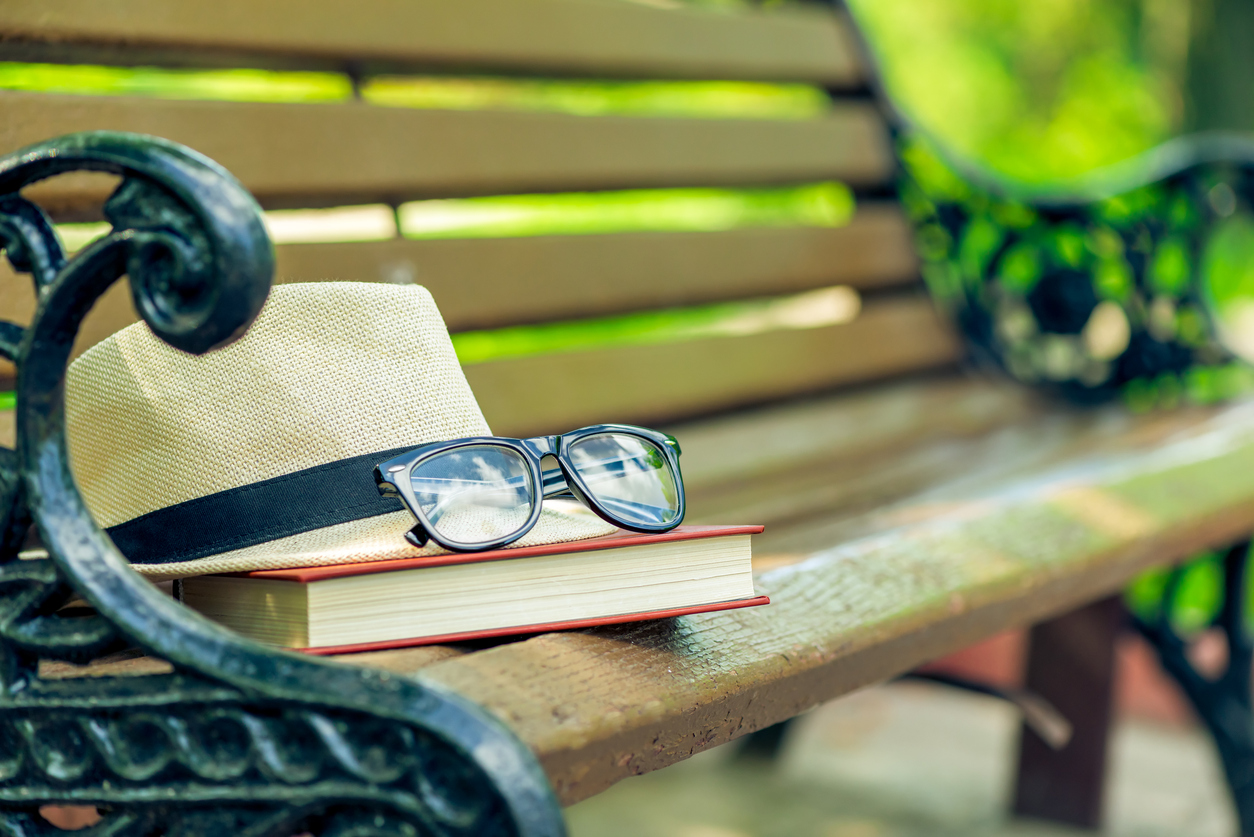 a forgotten book, a hat and glasses lie on the edge of a bench in a summer park
